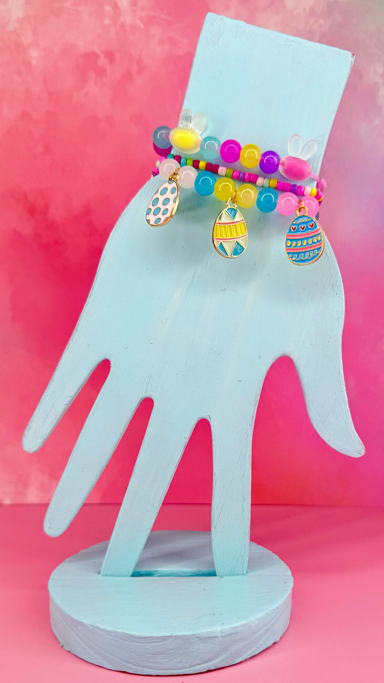 Stacked pastel bead bracelets with colorful egg charms on blue hand display