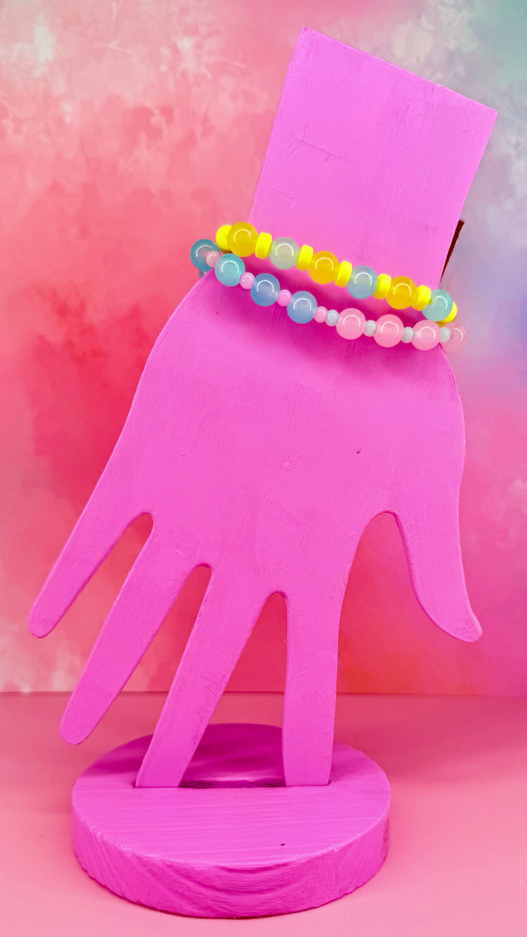 Stacked pastel bracelets on a pink hand display with multicolored beads