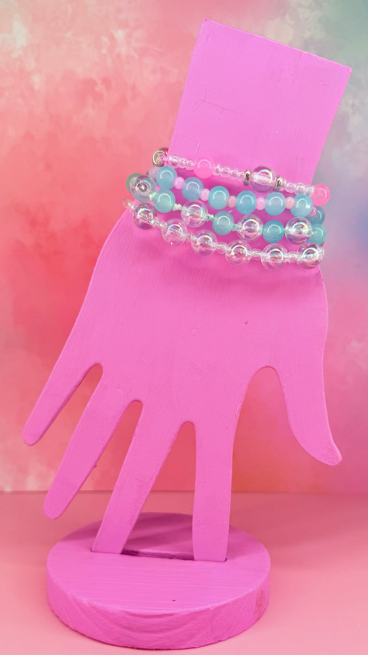Stacked blue and clear beaded bracelets on a pink hand display