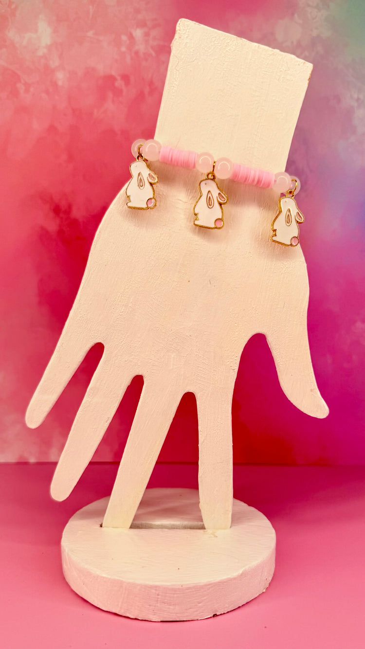 Pink beaded bracelet with three white bunny charms on hand-shaped display
