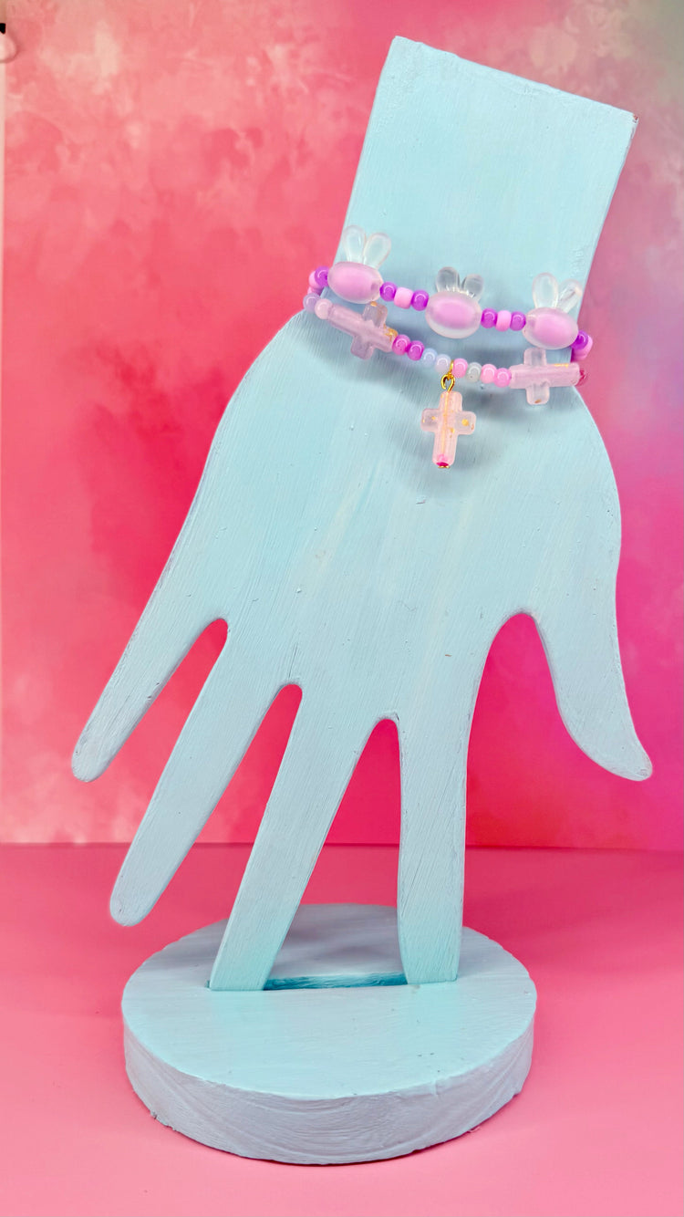 Layered bracelet set with pink bunny beads and cross charms on blue hand display
